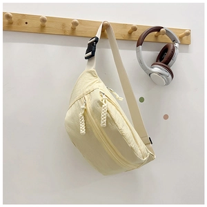 Detail of light yellow nylon chest bag featuring double zippers and cream woven strap