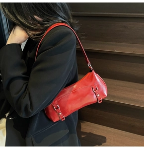 Side view of a glossy red baguette shoulder bag with silver hardware on a model