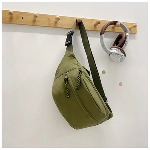 Detail of olive green nylon sling bag with woven zipper pulls on a wooden hook