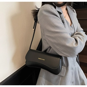 Detail of a black minimalist underarm bag with gold logo and slim shoulder strap