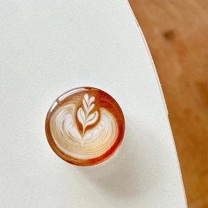 Detail view of a round 3D coffee latte art phone socket grip on a minimalist desk surface