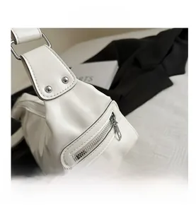 Detail shot of white shoulder bag featuring silver rivets and zipper pocket accents