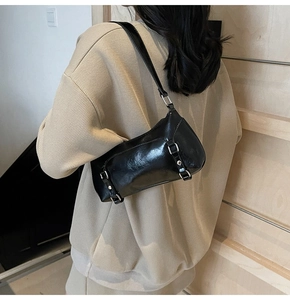 Detail of glossy black leather shoulder bag with silver buckle straps worn by a model