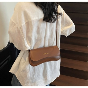 Brown leather crossbody bag with gold text detail worn over a white oversized shirt