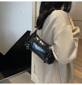 Close-up of black glossy leather underarm bag with silver buckles and metal rivets detail