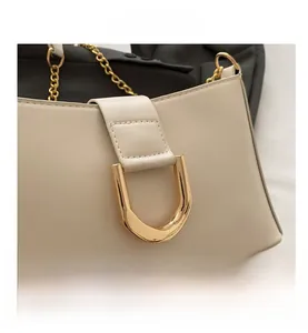 Close-up of beige leather shoulder bag with bold gold U-shaped buckle and chain strap