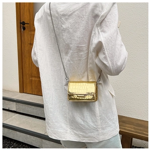 Detail shot of a golden crocodile texture mini crossbody bag worn over white blazer.