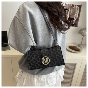Detail of black printed leather shoulder bag with gold M-logo turn-lock and adjustable strap