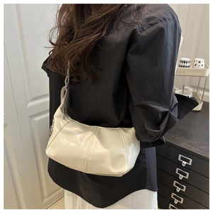 Detail of a creamy white glossy leather shoulder bag with vertical stitching and silver buckle