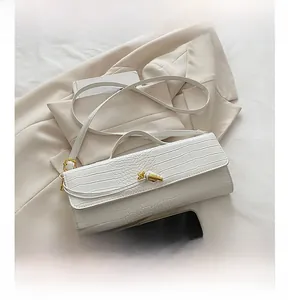 Detail of white crocodile pattern bag with golden knot hardware on a beige blazer background