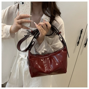 Detail of a shiny dark red dumpling bag featuring unique trapezoidal geometry and wide strap