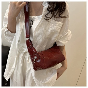 Detail of burgundy glossy leather shoulder bag featuring side zipper and wide strap