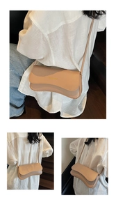 Close-up of cream crossbody bag with wavy flap design and metal embossed fashion text