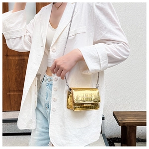 Small gold metallic square crossbody bag with chain strap worn with white blazer