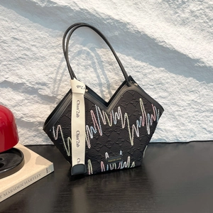 Grande borsa tote nera con ricamo a onde e tracolla in tessuto su sfondo in pietra