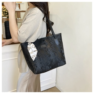 Detail of black snakeskin tote bag with elegant silk scarf and metallic logo plate