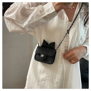 Detail of crossbody bag with black bow, floral silver buckle and quilted texture