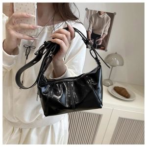 Detailed close-up of glossy black pleated leather texture and silver buckle on shoulder bag