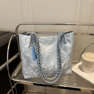 Blue butterfly jacquard tote bag with woven straps and tassel displayed on a metal rack