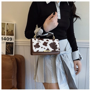 Female model carrying a stylish cow print small square handbag with a gold chain strap.