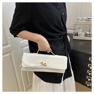 Detail of white crocodile embossed handbag with a golden twist knot clasp and leather strap