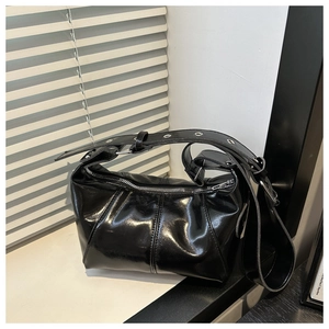 Detailed texture of black glossy leather shoulder bag with pleated finish and silver eyelets