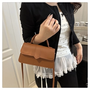 Detail of a brown leather handbag featuring a unique V-shaped flap and dual carry handles