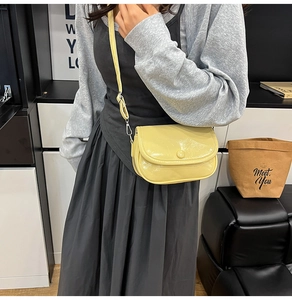 Detailed close-up of a pale yellow glossy crossbody bag on a modern casual model