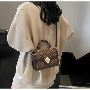 Deep brown crossbody bag with gold floral clasp and patterned texture shown with model