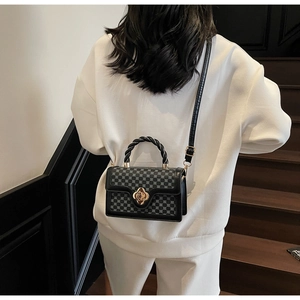 Detail of grid pattern handbag featuring golden clover lock and braided handle on model