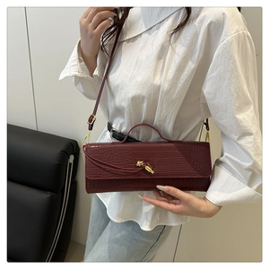 Detail of burgundy crocodile-embossed bag with gold-tone knot buckle and long strap