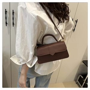 Detail of dark brown leather square crossbody bag with gold-tone hardware and top handle