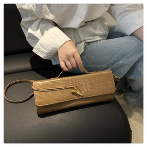 Detail of brown crocodile pattern baguette bag with gold metal buckle held by model