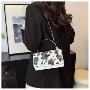 Detail of a stylish cow-print handbag featuring a gold metal handle and chain strap
