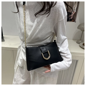 Detail of matte black leather underarm bag with gold horseshoe buckle and chain strap