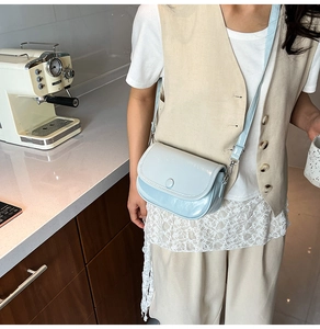 Close-up of a light blue saddle bag with a round buckle worn as a crossbody purse