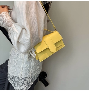 Detail of a bright yellow flap bag with FASHION lettering and a lace pearl charm