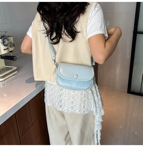 Pale blue faux leather saddle bag worn by a model in a modern cafe setting