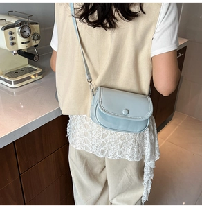 Detail view of a pale blue crossbody bag worn by a model in a cozy minimalist setting