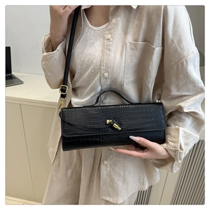 Detail of black crocodile embossed baguette bag with golden twist lock and sleek texture