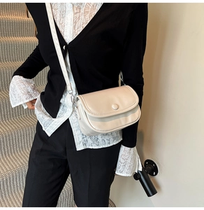 Detail of a creamy white minimalist crossbody bag with adjustable strap and metal hardware
