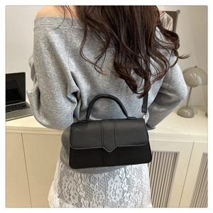 Detail of minimalist black leather crossbody bag with curved handle and sleek strap
