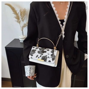 Modelo con bolso con estampado de vaca, asa de metal dorado y detalle de correa cadena