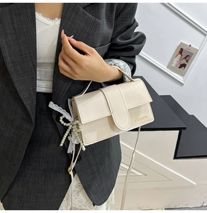 Detail of cream glossy leather handbag with fashion text and pearl bow ornament