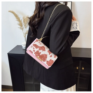 Detalle de bolso bandolera rosa con estampado de vaca y cadena dorada