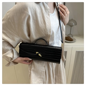 Detail of black crocodile texture baguette bag with golden metal knot buckle shown on model