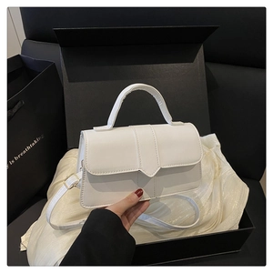 Detailed view of white faux leather crossbody bag with V-flap and gold buckle on gift box