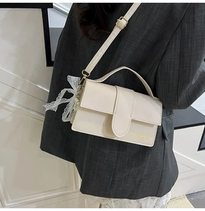 Detail of cream white crossbody bag with lace bow, pearl charm and gold fashion logo