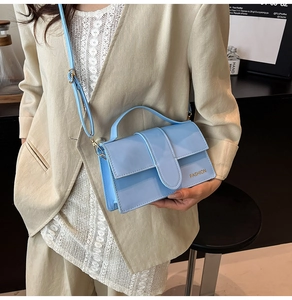 Detail of light blue patent leather handbag featuring gold Fashion lettering and top handle