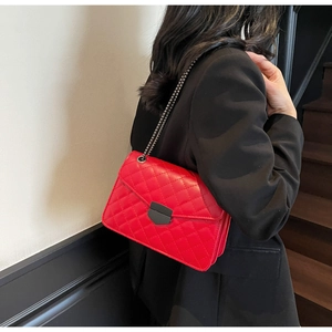 Détail d'un sac à bandoulière matelassé rouge avec chaîne sur blazer noir